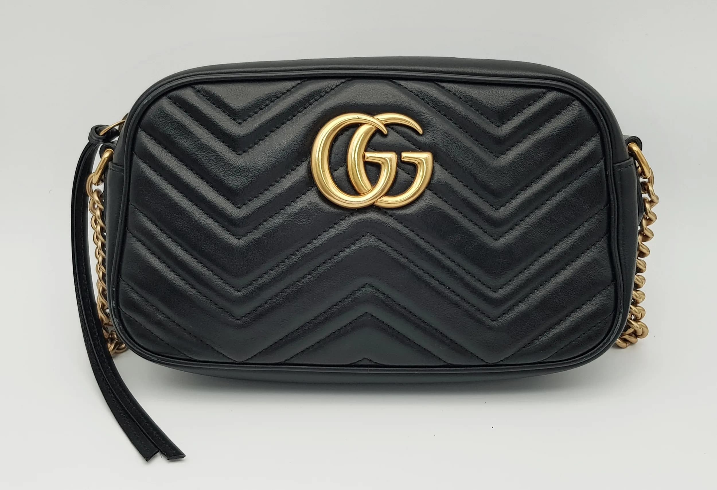 A Black Gucci Matelassé Leather GG Marmont Shoulder Bag. Black matelassé leather exterior with gold-tone hardware, featuring the iconic GG logo to front, adjustable leather shoulder strap and zipped top closure. Beige textile interior with a single main compartment and inner slip pocket. Some signs of wear, stains and mark to the leather. Comes with box, dust cover, purchased receipt and care booklet. Approx 22cm length x 14cm height x 6cm depth. Please see photos or request a condition report. Ref: 27784.