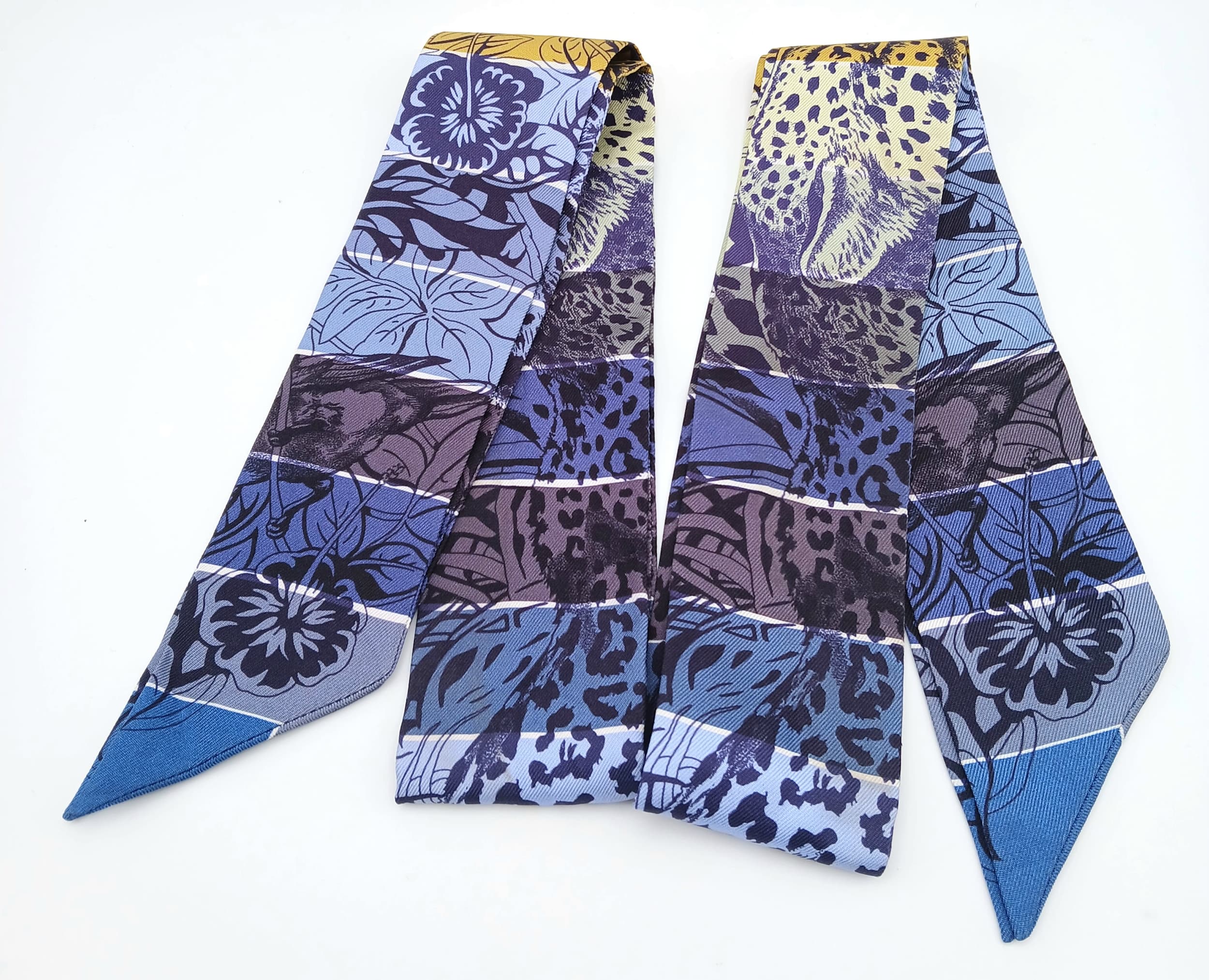 An Hermès “Jungle Love Rainbow” Twilly Silk Scarf.Multicoloured silk with jungle-inspired motifs in blue, yellow and purple tones. Approximate size: 84.5cm x 5cm. Ref: 27841
