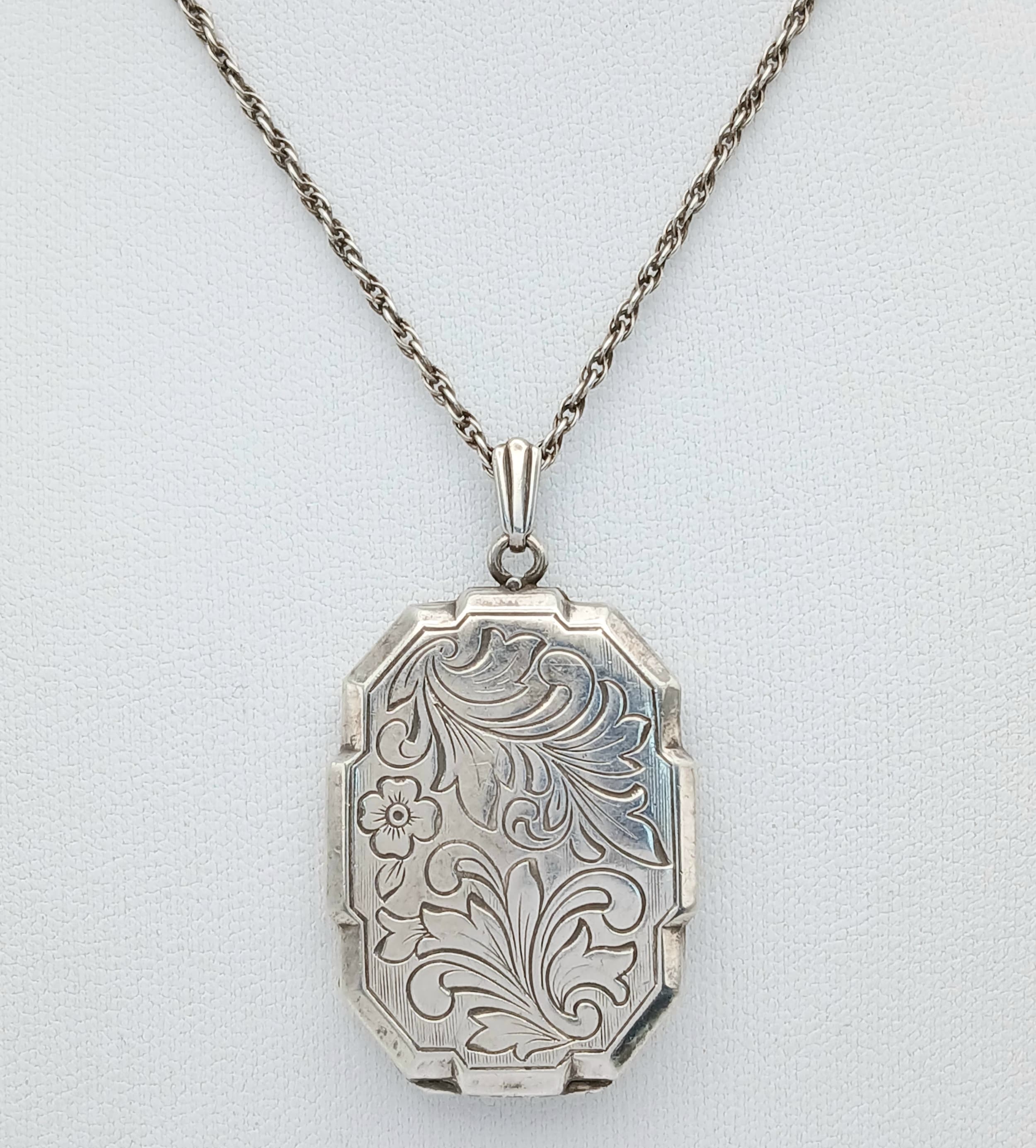A vintage sterling silver locket pendant with floral motif engravings, set on a silver necklace. Total weight 10.9G. Total length 54cm