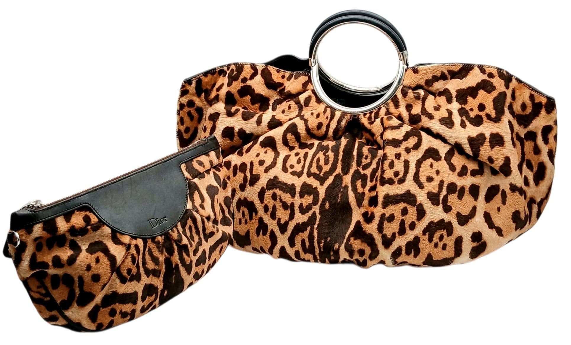 A Christian Dior Leopard Print Pony Hair Ring Handle Tote Bag. Leopard print pony hair exterior with silver-toned oversized circular top handles, protected base studs and open top design. Brown textile interior with one main compartment and an open side pocket. Approx 53cm length x 26cm height x 17cm depth. Comes with a matching leopard print zipped purse measuring approx 29cm x 11cm x 4cm. Some scratches to the leather and hardware but in good condition overall. Comes with a certificate of authenticity and dust cover. Please see photos or request a condition report. Ref: 28653.