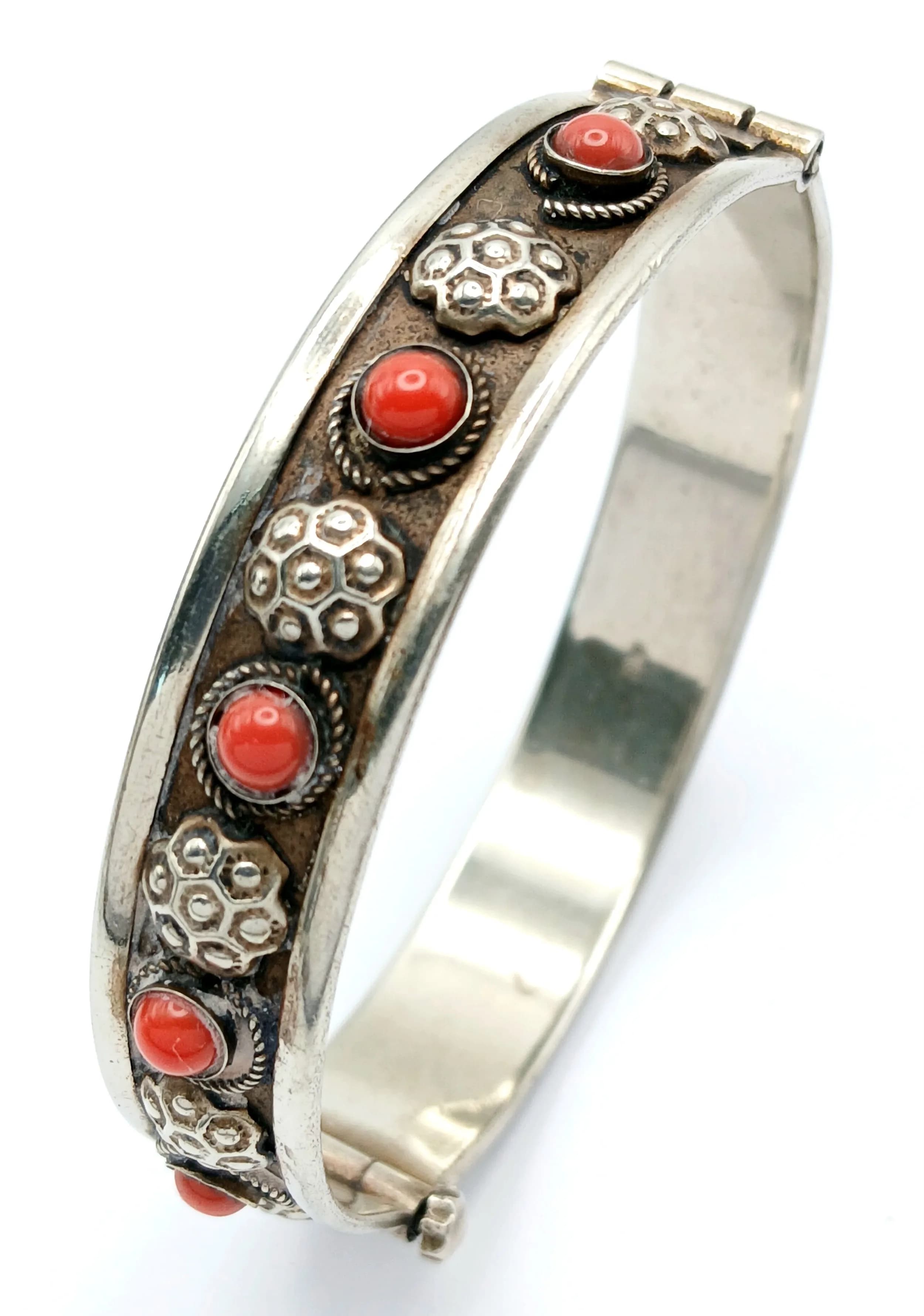 A Vintage Silver Coral Cabochon Set Hinged Bangle-6cm Diameter. The 10mm Wide Bangle features Round Coral Cabochons with Ornate Floral and Beaded Detailing. Gross weight 15.32 grams. Comes with a presentation box.