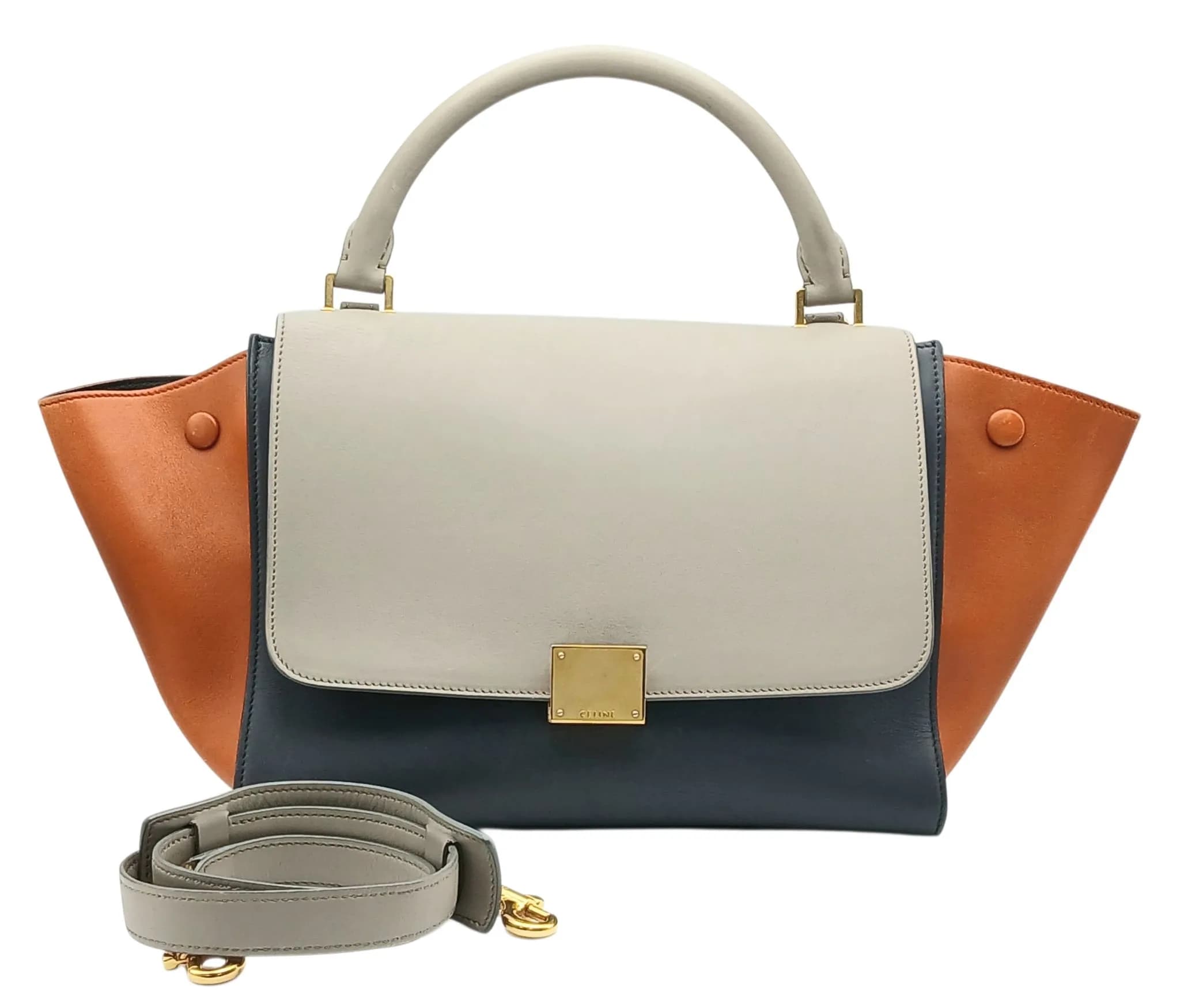 A Céline Smooth Calfskin Tri-Colour Trapeze Bag. Grey, brown and charcoal smooth calfskin leather exterior with gold-toned hardware, rolled top handle, detachable shoulder strap, rear zipped pocket and press-stud side details. The zipped top and front flap open to a charcoal leather interior with one main compartment, one zipped inner side pocket and two open inner side pockets. Comes with certificate of authenticity and a dust cover bag. Size approx: 45cm length x 20cm height. Some signs of creasing and minor scratches to the leather exterior. Please see photos or request a condition report. Ref: 26500