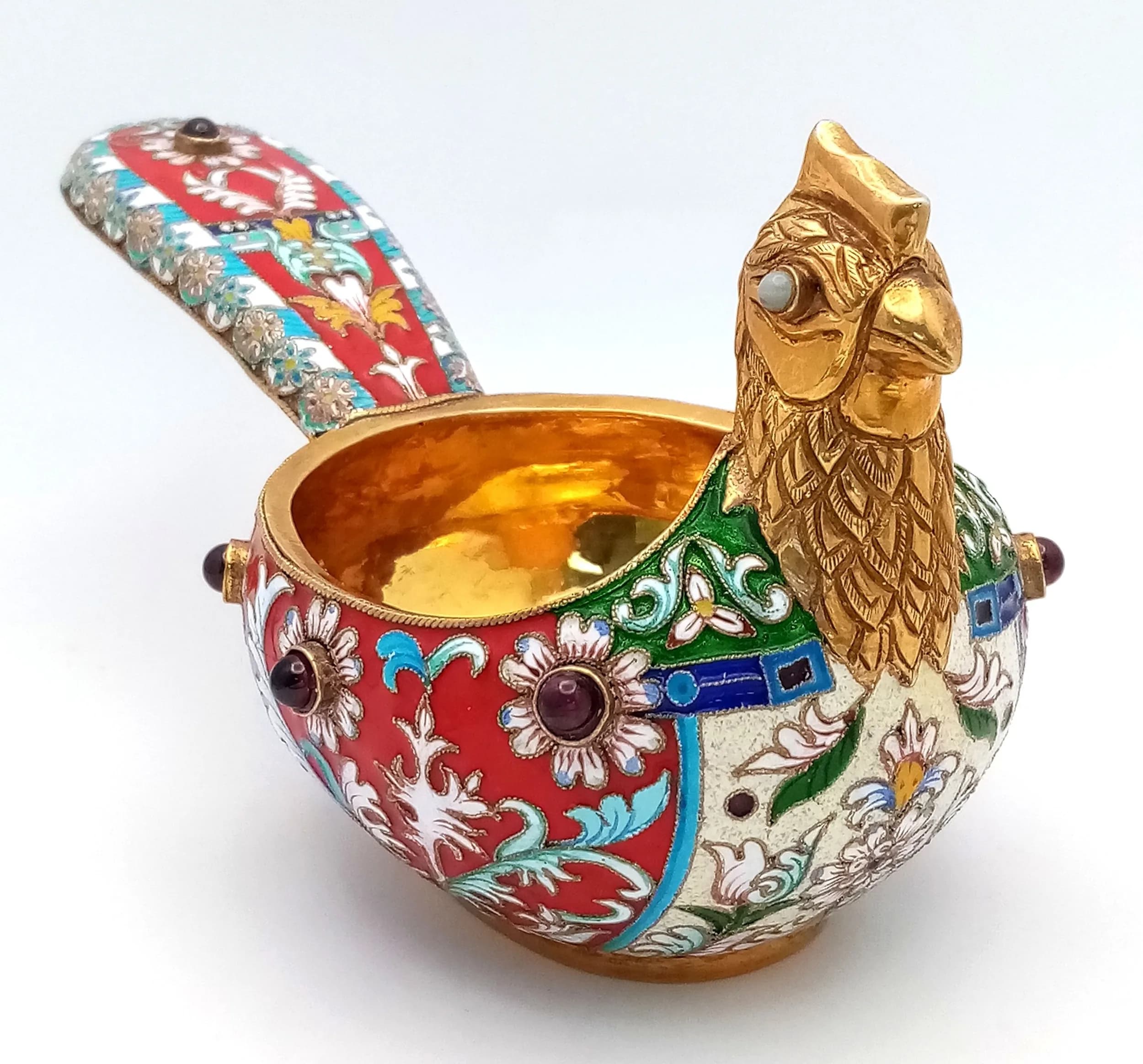 A Russian Style Gilded Silver, Enamel and Gem Set Bird Kovsh. Silver gilt and cloisonne enamel exterior set with ruby coloured cabochons (one ruby missing). Silver gilt interior. 13.5cm length x 7.5cm height. 143.6g total weight.