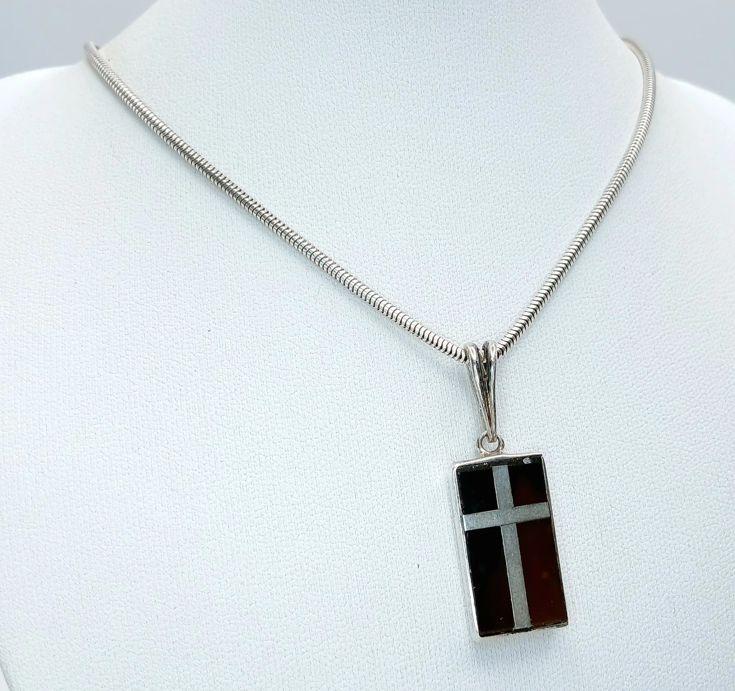 A Sterling Silver Silver Brown Tiger’s Eye Inlay Pendant Necklace. The pendant is set with brown tiger’s eye inlay with silver cross detail. Chain approx 40cm length. Pendant approx 2cm x 1.3cm. Total weight: 13.17g.