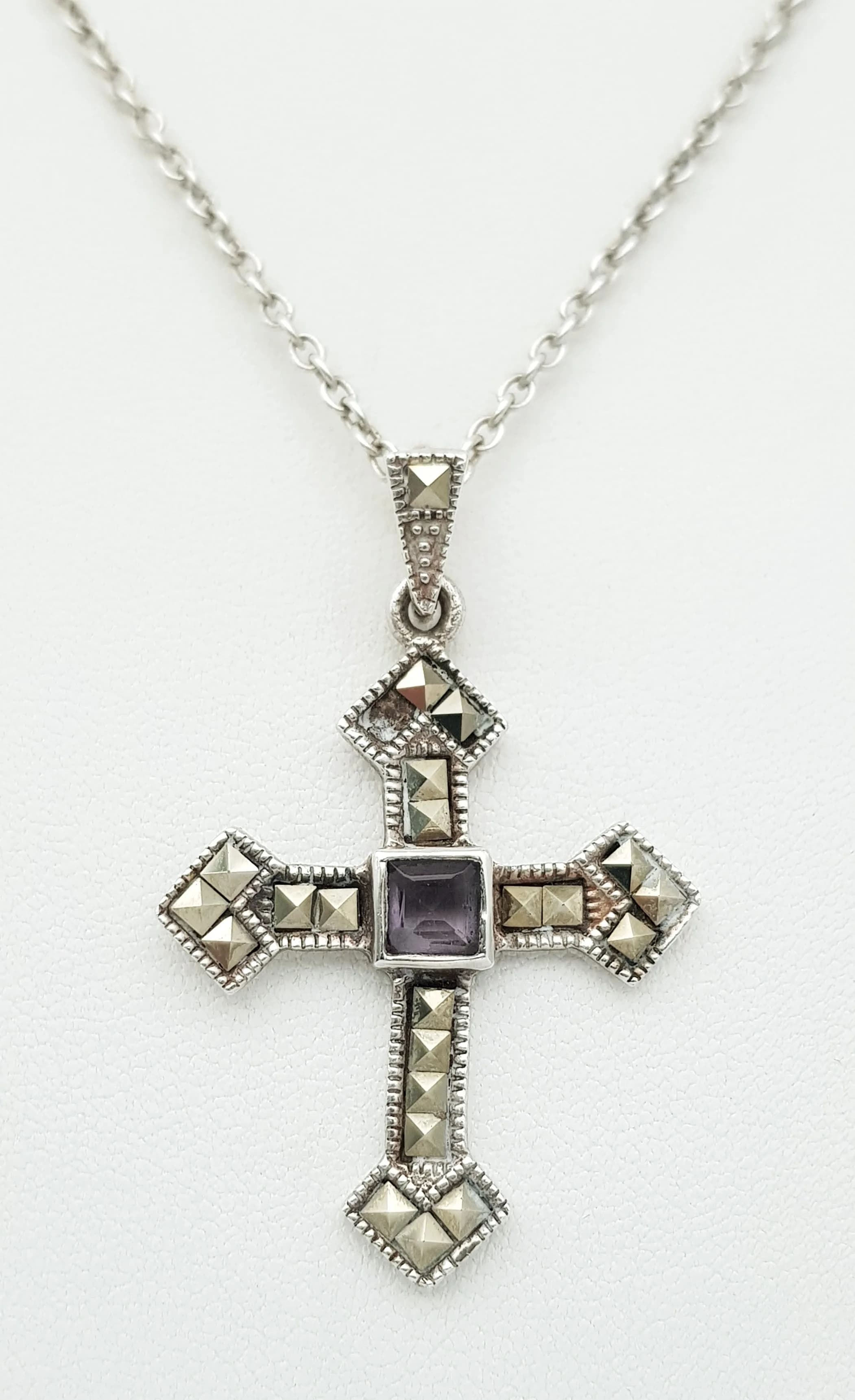 A Stunning 925 Silver Amethyst and Marcasite Cross Pendant Necklace. Set with a square cut amethyst centre stone and marcasite detail throughout the cross pendant, on a silver chain. Chain approx 48cm length. Pendant approx 4cm x 3cm. Total weight 8.17 grams.