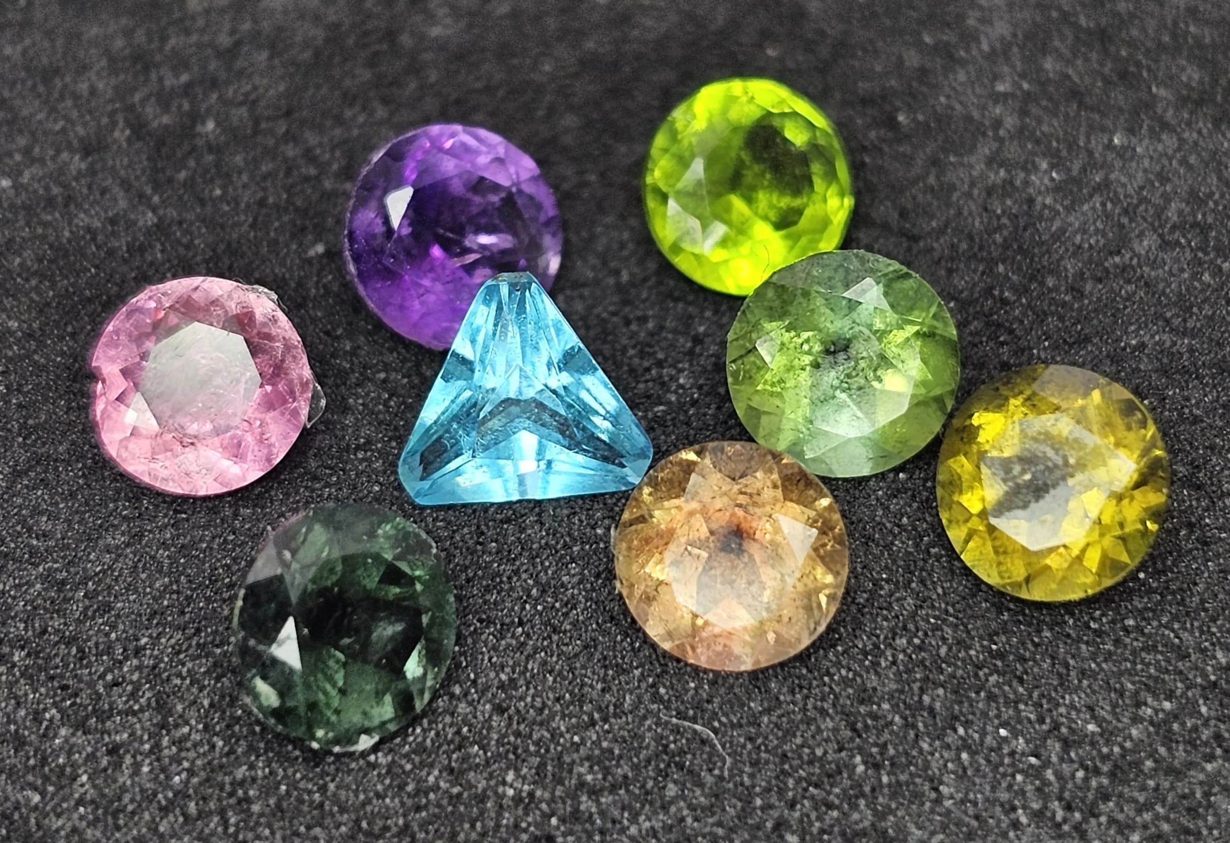 A Collection of Eight Semi-Precious 5mm Gemstones Ready for Mounting, Comprising of a Trillion Cut Blue Topaz and Round Cut Watermelon Tourmaline, Olive Tourmaline, Green Tourmaline, Pink Tourmaline, Blue Tourmaline, Amethyst and Peridot. Each approximately 0.5 carat